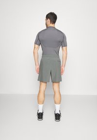 Conjunto desportivo masculino: t-shirt justa de manga curta cinza e calções verdes-oliva até ao joelho; cores sólidas, tecido leve, cintura elástica.