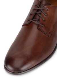 Brūna ādas vakara kurpe ar gludu tekstūru, smailu purngalu un tradicionālu auklu aizdari. Satur diskrētu zīmolu uz sāniem.