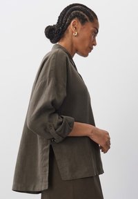 Khaki linen shirt with a loose fit, rolled sleeves, side slits, and a notched collar. Smooth texture with a matte finish.