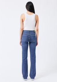 Pantalones vaqueros de mezclilla azul de corte acampanado con una cintura alta, con un acabado ligeramente texturizado, dos bolsillos traseros y costuras en contraste.