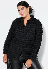 Blusa nera testurizzata con chiusura a bottoni, caratterizzata da un motivo peloso e un colletto classico, abbinata a pantaloni in faux pelle nera lucida.
