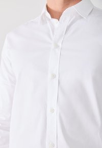 White button-up shirt made of smooth cotton, featuring a classic collar, front buttons, and a fitted design. No patterns or accents noted.