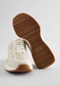 Chaussures de sport beiges avec une tige en mesh, des accents en suède et une semelle en caoutchouc marron dotée d'un motif de crampons texturé. La marque est "NEXT".
