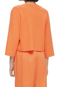 Orange cropped sweater with 3/4 sleeves, soft texture, and a simple, clean design. Worn over coordinating orange pants.