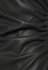 Svart läderstof med en slät textur, med insydda partier och subtila veck som skapar en dimensionell look.