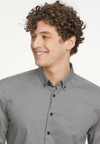 Camisa abotonada con un patrón geométrico en azul marino y crema, confeccionada en una tela suave, con cuello puntiagudo y botones oscuros.