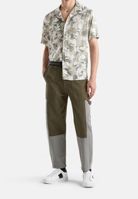 Camicia a maniche corte con un motivo floreale verde chiaro, abbinata a pantaloni cargo verde oliva e grigi. Le sneakers bianche completano l'outfit.