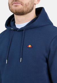 Sudadera azul marino de algodón, con un bolsillo frontal, capucha con cordón y un pequeño logo bordado en naranja y rojo.