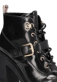 Schwarze Lackleder-Stiefelette mit einem stabilen Absatz, goldenen Hardware-Details, dicken schwarzen Schnürsenkeln und einer Schnallenverzierung an der Seite.