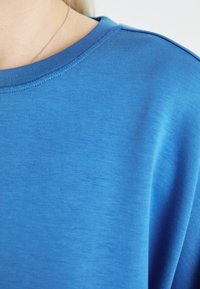 Kék pamut póló kerek nyakkal, sima textúrával és rövid ujjal, tiszta varrással a nyakvonal mentén és a vállaknál.