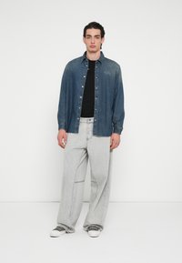 Sötétkék farmering gombos záródással és világoskék hímzéssel. Szürke, bő szárú nadrág finom varrási részletekkel, fehér sportcipővel.