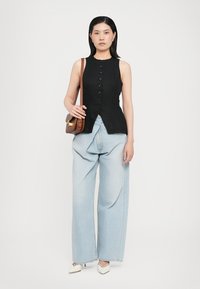 Black sleeveless top with button accents, paired with loose light blue jeans. Simple brown crossbody bag and pointed white shoes.
