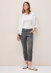Pantalones gris ajustados con una textura suave, bolsillos delanteros y costuras. Combinados con una camisa blanca y zapatillas gris claro. Diseño simple.