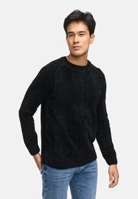 Maglione nero lavorato a maglia con scollo rotondo a coste e motivo testurizzato, abbinato a jeans azzurri chiari. Tessuto morbido e spesso con vestibilità rilassata.
