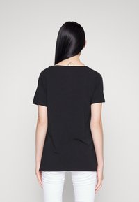 Černé tričko s krátkým rukávem s texturovanými detaily na ramenou a volným, uvolněným střihem. Spárované se slim-fit bílými džíny.