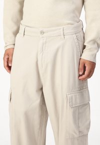Pantaloni cargo bej cu închidere prin buton, buzunare laterale și croială relaxată. Realizați dintr-un material durabil, cu o textură netedă și cusături în contrast.