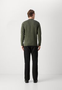 Donkergroen gebreid trui met ronde hals, geribbelde manchetten en zoom, gecombineerd met zwarte rechte broek en zwarte schoenen.