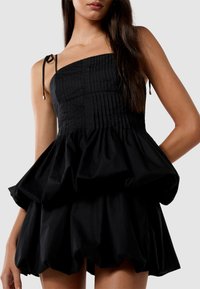 Robe noire avec un corsage plissé et une jupe évasée à volants. Comprend des bretelles fines et ajustables et une texture lisse.
