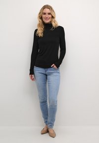 Melnas garas piedurknes turtlenecks, apvienots ar gaiši ziliem šaurajiem džinsiem un bēšiem apaviem, ar brīvu piegriezumu un mīkstu audumu.