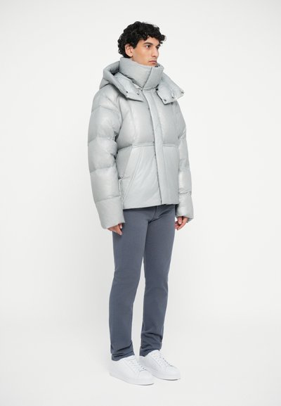 Silver puffer jacket with a high collar and large hood, featuring a quilted design and wide sleeves; worn with gray pants and white sneakers.