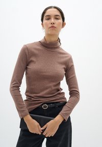 Barna bordás garbó, hosszú ujjal, fekete magasan derekú nadrággal és fekete clutch táskával párosítva, arany díszített övvel.