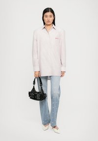 Camisa oversized às riscas vermelhas e brancas, calças de ganga azul claras com detalhes florais e uma pequena carteira preta. Sapatos de salto brancos em bico.