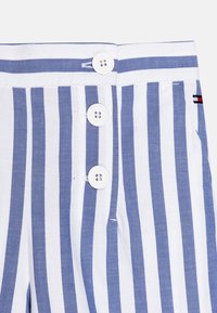 Blauwe en witte gestreepte broek met knoopsluiting, met drie witte knopen bij de taille en een klein merkembleem aan de zijkant.