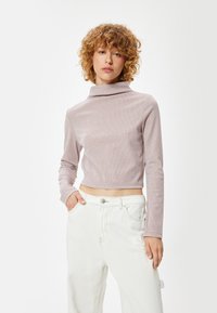 Lichtpaarse geribbelde turtleneck top met lange mouwen, cropped lengte en zachte textuur, gecombineerd met witte high-waisted broek.