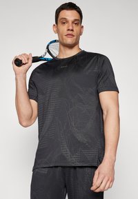 Must have mustakateeline sport särk, millel on geomeetriline mustrikujundus ja mis on valmistatud siledast kangast. Lühikesed varrukad, ümmargune kaelus ja väike logo rinnal.