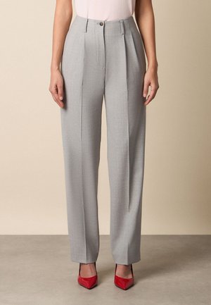 Jasnoszare, wysokowysoko taliowane spodnie z przodu z zakładkami, noszone z czerwonymi szpilkami z ostrym czubkiem i białą bluzką.