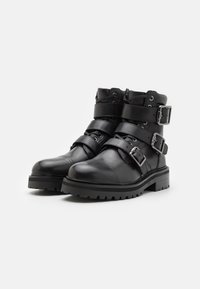 Botas de cuero negras hasta el tobillo con tres correas anchas, hebillas de plata, punteras redondeadas y suelas robustas con tacos de tracción.