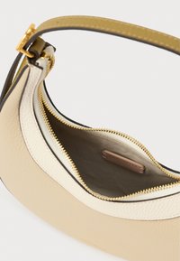 Mala em couro bege e creme com fecho dourado e alça curta, mostrando o interior aberto com uma etiqueta de marca no interior.