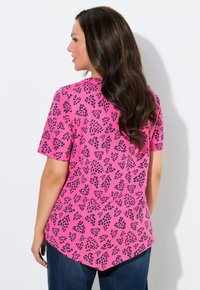 T-shirt rosa a maniche corte con motivo a foglie nere, orlo arrotondato e vestibilità comoda. Il tessuto sembra morbido con una texture liscia.