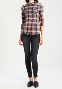 Camicia a quadri con sfumature di grigio, arancione e nero, con chiusura a bottoni sul davanti e due tasche sul petto, abbinata a jeans skinny neri e ballerine nere.