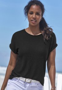 Mustaline, lühikeste varrukatega, tekstuuriga pullover koos ümmarguse kaelusega, kantud valgete pükste ja valge vöödiga. Väljas taust, sinine taevas.