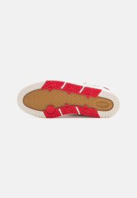 Shoe sole featuring a white rubber base, red accents, and textured hexagonal patterns. Includes circular grip elements and traction grooves.