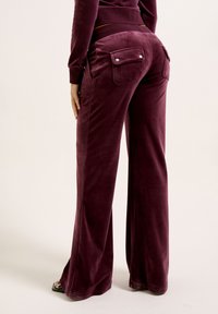 Bordeaux fluwelen broek met brede pijpen, voorzien van voor- en achterzakken, met glanzende zilveren knopen en een soepele textuur, vanuit de achterkant weergegeven.