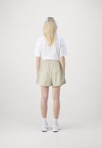 Short beige avec une ceinture élastique, associé à un t-shirt blanc. La personne porte des cheveux blonds, raides et mi-longs. Des baskets blanches complètent la tenue.