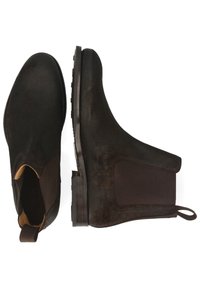 Bottes de cheville en suédine marron foncé, avec des empiècements latéraux élastiques, une semelle en caoutchouc texturée et une languette pour un enfilage facile.