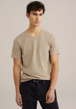 Beige bomulds t-shirt med kortærmer og V-hals på en model, parret med mørke jeans. Stoffet ser glat ud, med en afslappet pasform.
