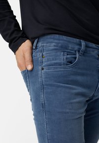 Blaue Cordhosen mit schmaler Passform, fünf Taschen und dezenten Steppnähten. Der Stoff hat eine weiche Textur mit leichtem Glanz.