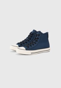 Et par marineblå høyhælte kanvas sneakers med hvite gummisåler og svarte snørebånd på en lys grå bakgrunn.