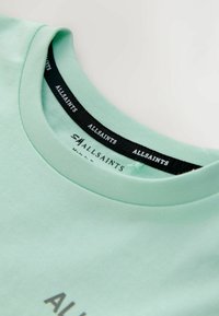 Mintgrøn bomulds-T-shirt med rund halsudskæring og et sort mærke med teksten "ALLSAINTS" trykt inde i halskanten.