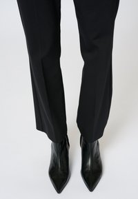 Czarne, dopasowane spodnie o prostym kroju, zestawione z czarnymi, błyszczącymi botkami z ostrym noskiem. Minimalistyczny design z eleganckim wykończeniem.