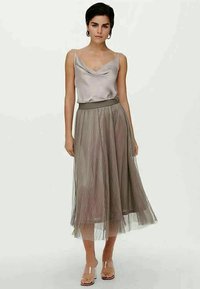 Satin-grauer Cowl-Neck-Top kombiniert mit einem gefältelten, knielangen grauen Tüllrock. Klare Sandalen mit Blockabsatz runden das Outfit ab.