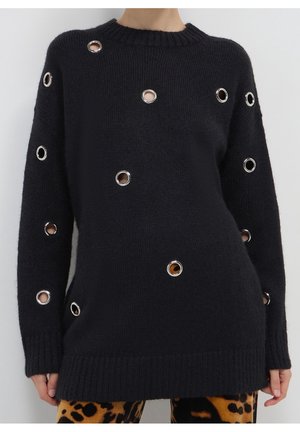 Pull en maille noire avec plusieurs œillets ronds argentés et coupe décontractée, associé à un pantalon imprimé léopard.