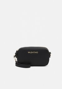 Black vegan leather crossbody bag with a zip closure, gold-tone logo, adjustable strap, and smooth texture. Compact rectangular shape.