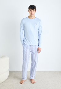 Vaaleansininen pitkähihainen paita pienellä logolla, yhdistettynä sinivalkoisiin raidallisiin pyjama-housuihin. Pehmeä kangas ja rento istuvuus.