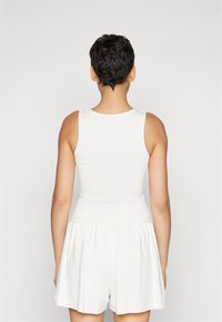Robe blanche sans manches avec un haut ajusté et une jupe évasée et froncée. Tissu doux à la texture lisse, design minimaliste, sans motifs visibles.