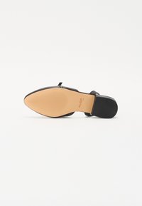 Chaussure fermée noire à bout rond avec un talon plat, dotée d'un dessus lisse et d'une semelle texturée couleur marron clair. Conçue avec une esthétique minimaliste.